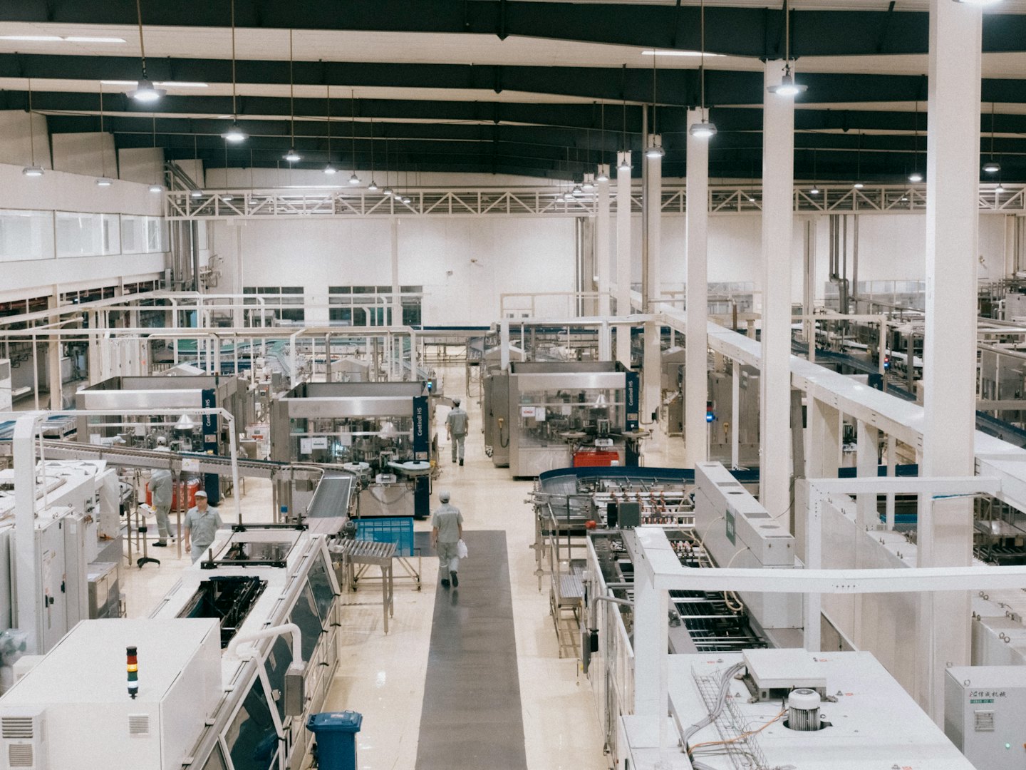 Pracownicy przemieszczający się między zautomatyzowanymi maszynami na linii produkcyjnej.